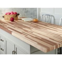 a large wooden cutting board sitting on top of a kitchen counter next to a basket of apples