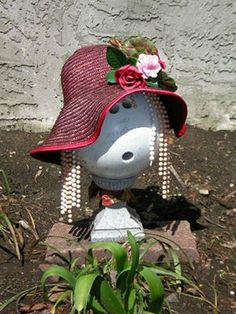 a statue of a person wearing a hat with flowers on it, sitting in the dirt