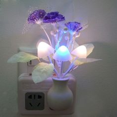 a white vase filled with purple flowers on top of a wall mounted outlet plugged in