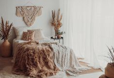 a bed with fluffy blankets and pillows on top of it next to potted plants