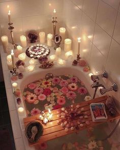 a bathtub filled with lots of candles next to a table and flowers on the floor