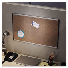 an office cubicle with a laptop, phone and other items on the counter top