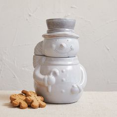 a snowman cookie jar with cookies in front of it and a white wall behind it