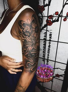 a woman with a butterfly tattoo on her arm and shoulder is standing in front of a wall