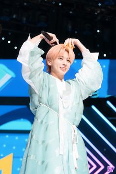 a woman in a blue dress is holding her hands up to her head while standing on stage