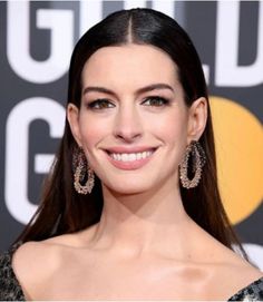 a woman with long dark hair wearing large earrings and smiling at the camera while standing in front of a golden globe award