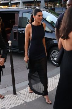 a woman in a black dress is walking down the street