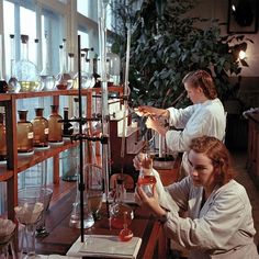 two women in white lab coats working with beakles and flasks on shelves