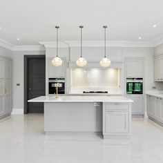 a large kitchen with white cabinets and marble counter tops, along with two pendant lights hanging from the ceiling