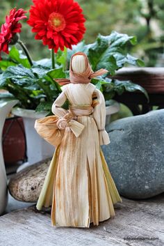 a figurine of a woman in a dress and hat is standing next to some flowers