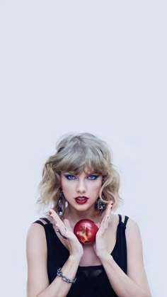 a woman holding an apple in front of her face with both hands and wearing red lipstick