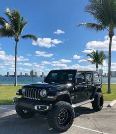 a black jeep parked in a parking lot next to palm trees and the ocean on a sunny day