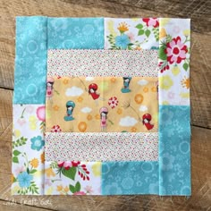 a patchwork quilt on top of a wooden table with flowers and clouds in the background