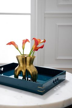 two gold vases with red flowers in them on a blue tray sitting on a white table