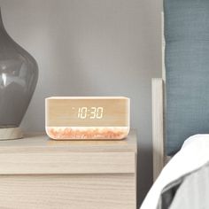 an alarm clock sitting on top of a nightstand next to a vase and bed headboard