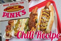 two hot dogs with toppings are on a tray next to a sign that says pink's chili recipe