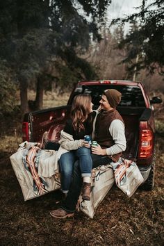 two people sitting in the back of a pickup truck with bags on it's bed