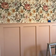 a chair sitting in front of a wall with flowers on it and a ladder leaning against the wall