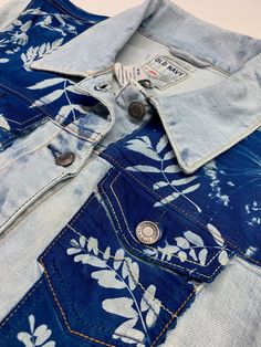 a blue jean jacket with white flowers and leaves on the front, buttoned down