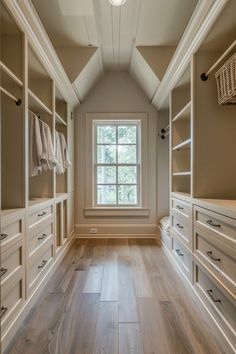 an empty walk in closet with wooden floors and white cabinets, along with large windows