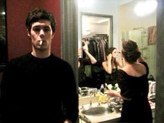 a man standing in front of a bathroom mirror brushing his teeth and looking at himself in the mirror