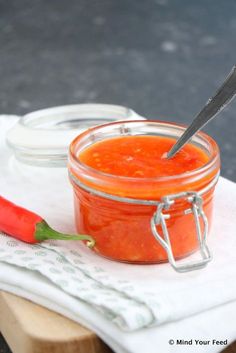 a glass jar filled with red sauce next to a knife and napkin on top of a cutting board