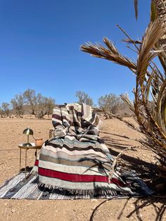 a blanket sitting on top of a rug in the middle of a dirt field next to a chair