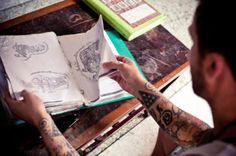 a man sitting at a table with some tattoos on his arm and an open book in front of him