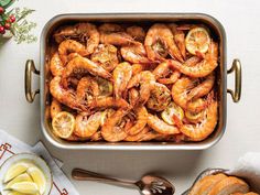 a pan filled with cooked shrimp next to sliced lemons and bread on a table