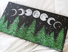 a painting with trees and the moon on it is sitting on a white bed sheet