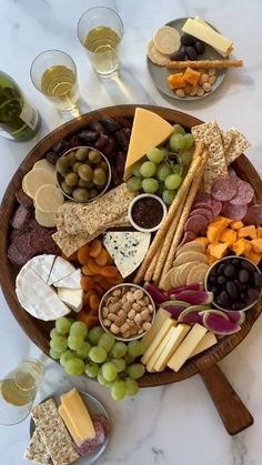 a wooden platter filled with cheese, crackers and grapes