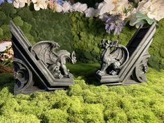 two dragon bookends sitting on top of moss covered ground next to white flowers