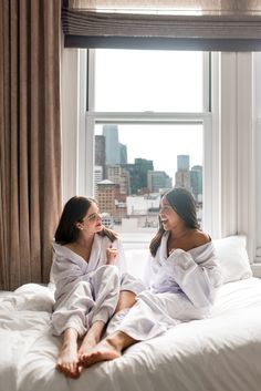 two women in white robes sitting on a bed