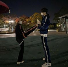 two people wearing face masks standing in front of an umbrella at night, one holding the leg of another person's leg