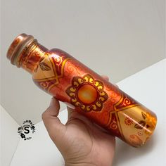 a hand holding an orange and red glass bottle with gold designs on it's side