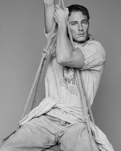 a man sitting on top of a wooden chair holding a rope over his head and looking at the camera