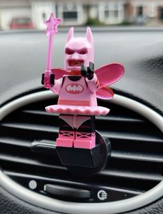 a pink lego batman character sitting on top of a car dash board in the dashboard