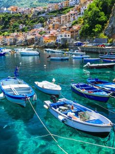 many small boats are docked in the clear blue water next to an island with houses on it