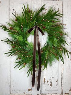 a green wreath hanging on the side of a white door with brown ribbon and pine cones