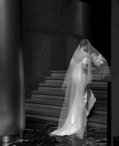 the bride is walking down the stairs in her wedding dress with a veil over her head