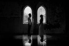 a man and woman standing in front of two windows with the light shining through them