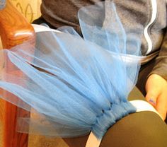 a person sitting on a wooden chair with a blue tulle around their waist and leg