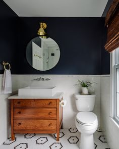 a white toilet sitting next to a wooden dresser in a bathroom under a round mirror