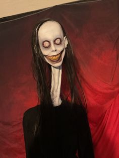 a creepy woman with long hair and makeup is standing in front of a red backdrop