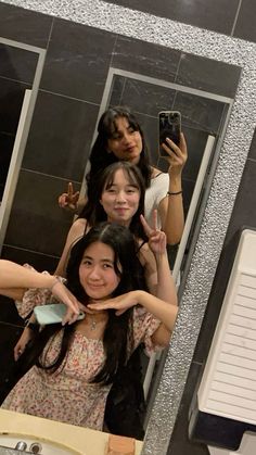 three women standing in front of a bathroom mirror taking a selfie with their cell phones