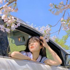 a woman sitting in the back seat of a car with cherry blossom on trees behind her