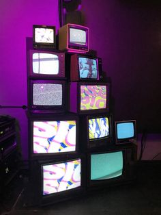 several televisions stacked on top of each other in front of a purple wall with neon lights