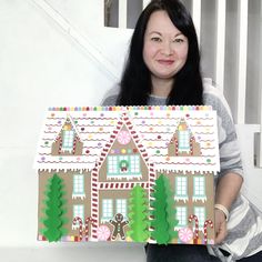 a woman holding up a cut out of a gingerbread house