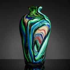 a colorful glass vase sitting on top of a black table next to a gray wall