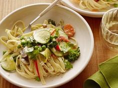 two bowls filled with pasta and veggies on top of a wooden table next to glasses